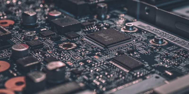 Sebuah fotografi tajam Lensa Makro membedah komponen kecil di atas Papan Induk motherboard komputer penuh silikon kawat hijau dan tembaga IC rumit